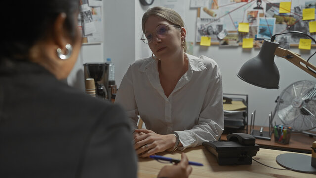 Two women engage in serious discussion in a cluttered investigation office with visible case evidence.