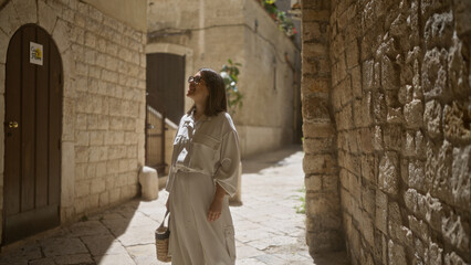 Young hispanic woman strolling through the old town streets of bari, italy, basking in the warm sunlight against ancient stone walls.