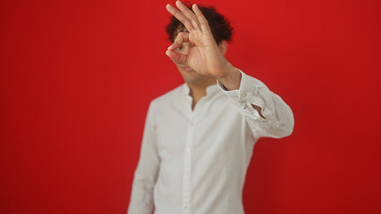 A young hispanic man in a white shirt over isolated red background making ok gesture