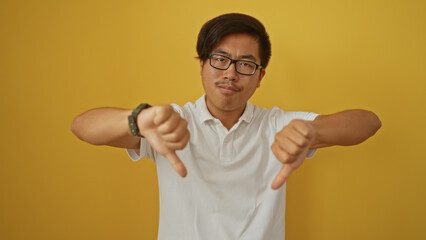 Fototapeta premium Young attractive chinese man showing thumbs down gesture over isolated yellow background