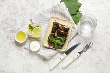 Plate with tasty Dolmas (stuffed grape leaves), sour cream, lemon slices, oil and glass of water on light background