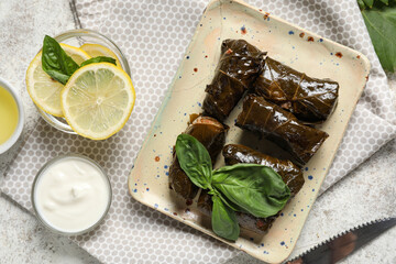 Plate with tasty Dolmas (stuffed grape leaves), sour cream and lemon slices on light background