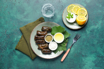 Plates with tasty Dolmas (stuffed grape leaves), spices, sour cream, lemon and glass of water on color background