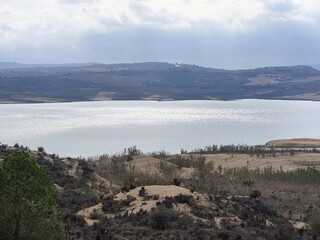 Stausee in einer kargen Landschaft, umgeben von felsigen Hügeln. Der sonnenschimmer auf dem Wasser...
