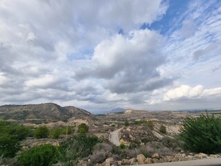 Typisch spanische Landschaft mit sanften Hügeln, etwas grünem Bewuchs und einem dramatischen Wolkenhimmel.