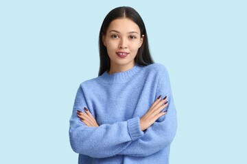 Beautiful young woman in light blue knitted sweater on color background