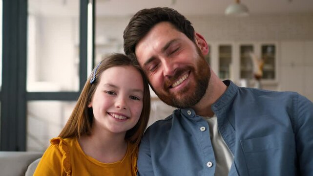 Smiling family portrait joyful Caucasian man father parent daddy guy male dad touch positive schoolgirl kid little girl daughter child looking at camera healthy white teeth at home childcare adoption