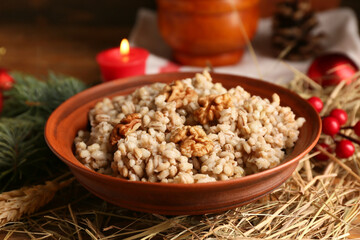 Bowl of traditional Ukrainian Kutya dish with Christmas tree branch and burning candle on wooden background, closeup