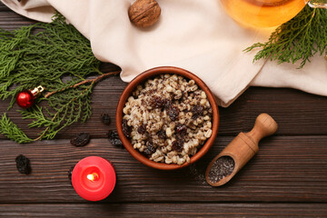 Bowl of traditional Ukrainian Kutya dish with coniferous branches and burning candle on wooden background