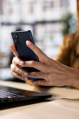 Professional woman checking her smartphone for business emails and project updates while multitasking at her desk. Female executive employs mobile technology to meet deadlines. Close up.
