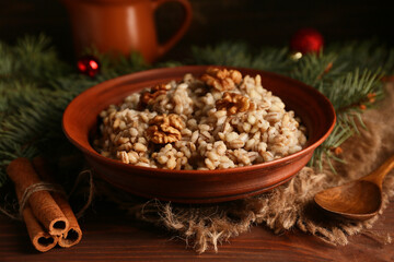 Bowl of traditional Ukrainian Kutya dish with cinnamon and Christmas tree branches on wooden background