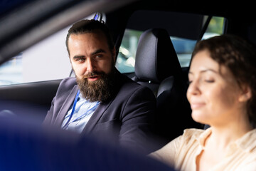 Car dealership sales executive with customer in car during test drive, discuss her needs, presenting deal offers. Smiling woman participating in test drive chatting with dealership salesman