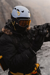 Videographer wearing a helmet, goggles, and gloves operates a professional camera in a cold, mountainous environment
