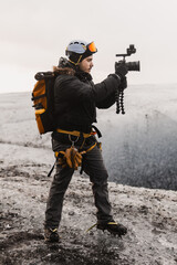 Content creator is recording video footage on a glacier using a gimbal and camera, wearing crampons for safety