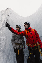 Two mountain guides wearing safety equipment and pointing at ice formation inside glacier crevasse...