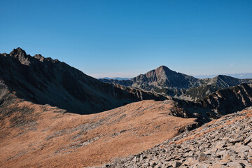 Majestic mountain range under a clear blue sky. Breathtaking panoramic view of rocky peaks and valleys. Perfect for travel, nature, and adventure themes.
