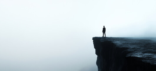 A person standing at the edge of a cliff, looking out over the foggy clouds. The person appears small and fragile against loneliness.