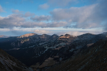 Majestic mountain range at dawn.  Clouds drift across a stunning vista of peaks and valleys, bathed in the soft light of sunrise. Breathtaking natural landscape photography.