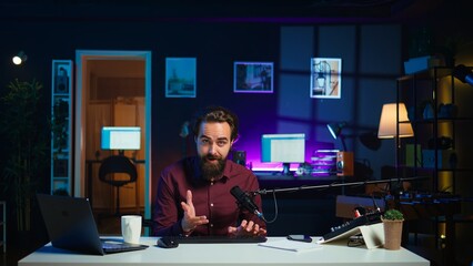 Man filming video for online channel in dimly lit home studio, presenting mouse and keyboard to...