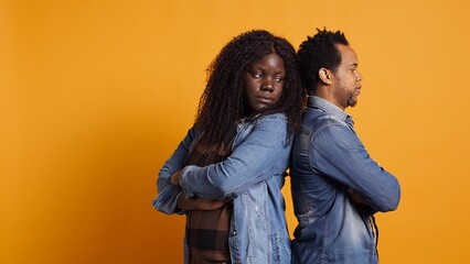 Fototapeta premium Distant sad husband and wife regret fighting each other in studio, standing back to back after a misunderstanding. African american couple with marriage problems, quarreling. Camera B.