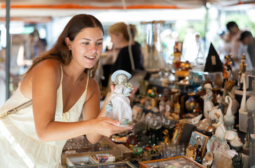 Satisfied interested young woman choosing interesting antique things at traditional flea market