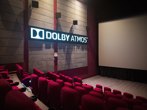 Empty Movie Theater With Dolby Atmos Sound System Display next to comfortable red seats and a large screen.