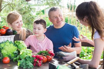 Parents with children relax at rustic table after harvesting ripe vegetables