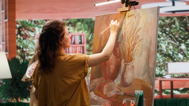 Skilled painter stands before a canvas painting a watercolor rustic artwork. Artist showing her skill and brush technique as she mixes dyes, creating a multicolored masterpiece. Camera A.