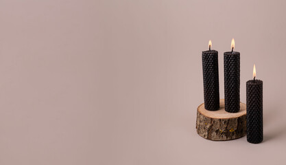 Three black textured beeswax candles stand on a wooden stand against a beautiful background.