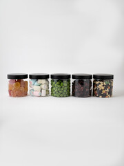 Collection of five transparent jars with different fillings of the same size on a white background