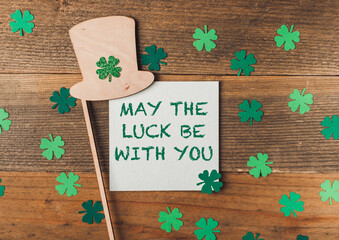 A green shamrock hat is on a wooden surface with a piece of paper