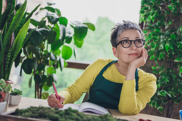 Photo of pensioner lady florist look dreamy empty space write notebook wear green apron working...