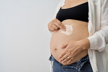 Pregnant woman applying cream on her belly, highlighting prenatal care and the importance of skin health during pregnancy in a minimalist setting