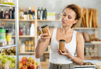 Female customer carefully choosing can of lentils in a grocery supermarket