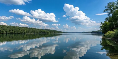 A serene blue sky with puffy white clouds is reflected in the calm waters of Brookville Lake on a warm summer day, summer landscape, idyllic setting