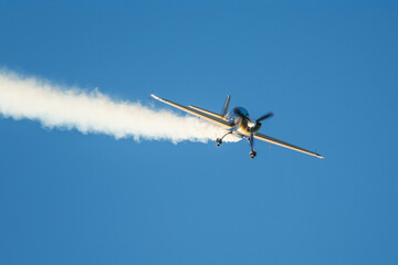 Golden stunt aerobatic plane performing stunts in blue sky with smoke trail. Concept of speed, difficulty, precision, risk