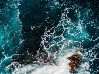 aerial of dark ocean waves crashing against the rocks creating whitewash 