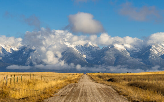 Old dirt road leading to snow covered mountains of Montana in winter with golden grass 