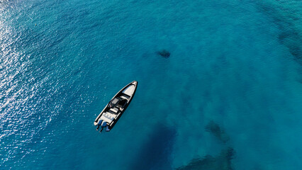 A sports boat is anchored in the middle of the sea with turquoise water from the top view of a drone