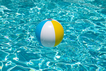 Beach ball floating in swimming pool. Advertising for summer vacations. Space for text. Colorful beach ball in swimming pool.
