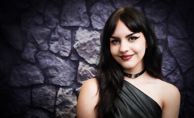 Fototapeta premium beautiful sexy gothic alternative female model with black hair smiling in front of stone wall