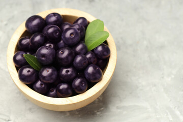 Ripe acai berries and leaves in bowl on grey textured table, closeup. Space for text