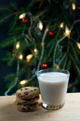 Glass of milk and cookies by a lit Christmas tree.