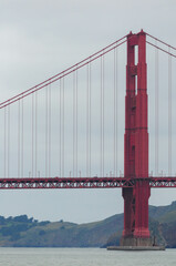 Red suspension bridge over calm bay with cloudy sky and green hills