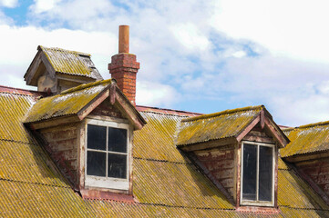 Weathered rooftop with rustic dormer windows, aged architecture under bright sky