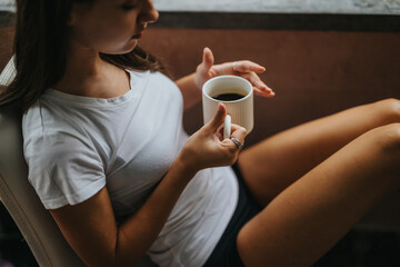 A young woman enjoys a peaceful moment with a cup of coffee, sitting comfortably at home. The scene...
