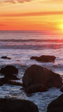 Atlantic ocean sunset with waves and rocks and surfers silhouettes in water at Costa da Caparica, Portugal. Camera pan