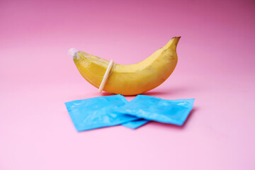 Yellow Banana And Condom Wearing It on Pink Background. The Concept of Safe Sex.
