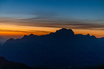 Sunset in the mountains. Red and orange burning sky horizon behind the alpine mountain range. Rocky mountain peaks of the Dolomites at sunset and dawn at sunrise light sunrays going through the clouds