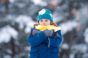 Happy teen child playing with snow during snowfall. Child in winter clothes, hat, gloves and scarf. Winter children play with snow. Happy winter holidays. Kid play with snowball. Winter kids portrait.